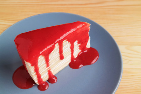 Slice of Delectable Vanilla Mille Crepe Cake with Bright Red Raspberry Sauceの写真素材