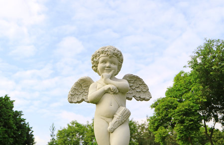 Adorable cupid sculpture in the garden against fluffy cloudy sky