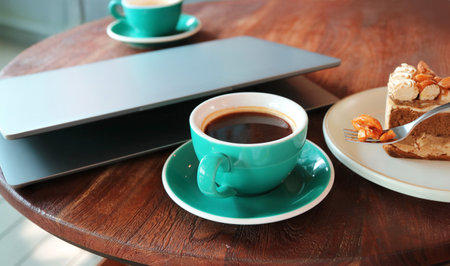 Cup of coffee and fork scooping candied nut with laptop in the backdropの写真素材