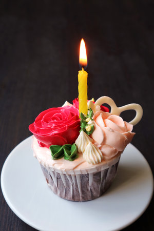 Gorgeous birthday cupcake decorated with rose bouquet shaped frosting and a shining candleの写真素材