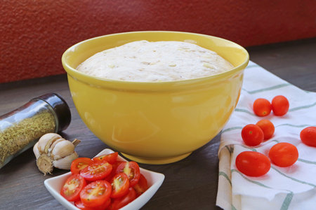 Bowl of proofed dough on the table surrounded with ingredients for bakingの写真素材