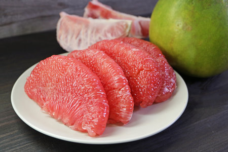 Mouthwatering Peeled Bright Red Pomelo Fruit Segments Lined Up on White Plateの写真素材