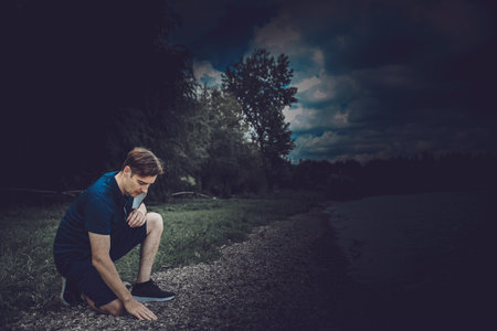 A guy wearing a black mask kneeling down and feeling the stones with his hand full of hope on the beach near lakesideの写真素材