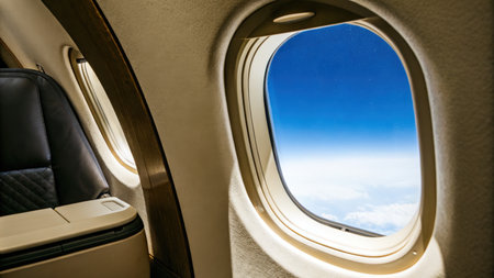 Airplane window seat view with a clear sky and distant cloudsの素材