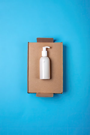 Top view of white cosmetic bottle on cardboard box on blue background.の素材