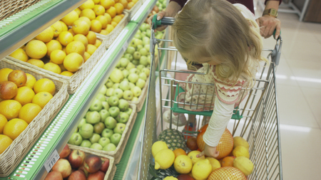 Family makes purchases in the supermarket. Mother and daughter choosing fruits and put them in the trolley.の写真素材
