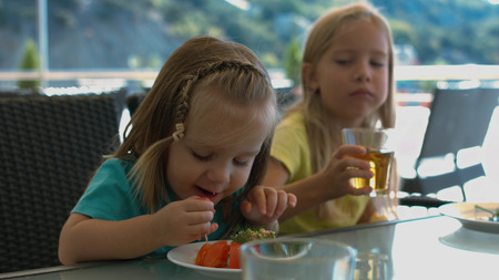 Two little sisters eating in the cafe outdoorsの写真素材