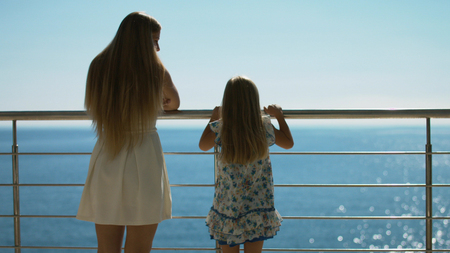 Mother and daughter standing on the outdoor terrace overlooking the sea, rear viewの写真素材