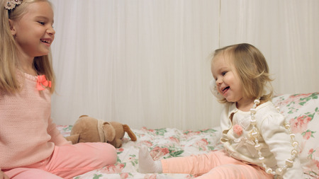 Cheerful little girls playing with beads on bedの写真素材