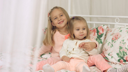 Two little sisters dressed in pink clothes sitting on the couchの写真素材