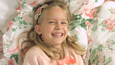Adorable little blonde girl lying on the bed and laughing gailyの写真素材