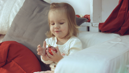 Little girl sitting on the couch and playing with the Christmas decorationsの写真素材