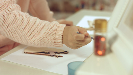 Little girl enthusiastically paints the wooden Christmas toy on the Christmas treeの写真素材
