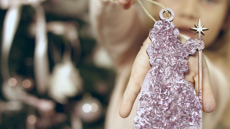 Beautiful blue-eyed girl hangs a homemade Christmas toy at the christmas treeの写真素材