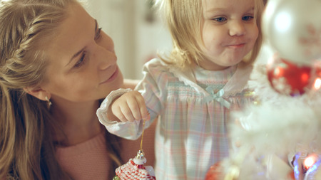 Little girl playing with Christmas toy near the Christmas tree with her mother