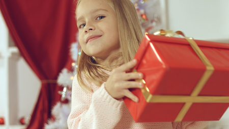 Blue-eyed little blonde girl is delighted from her New Year's gift wrapped in red paperの写真素材