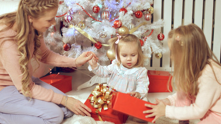 Family consists of females sitting around the Christmas tree with giftsの写真素材