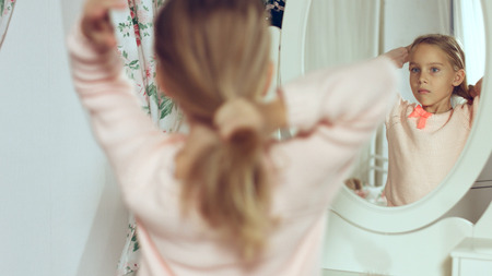 Fashionable little lady combing her blonde hair and looking in the mirrorの写真素材