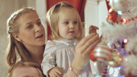 Mother with adorable baby decorate the Christmas tree at homeの写真素材