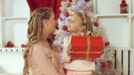 Mom gives gift to the daughter near the Christmas decorated treeの写真素材