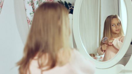 Fashionable little lady combing her blonde hair and looking in the mirrorの写真素材
