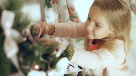 Cute little girl in pink sweater decorates the Christmas treeの写真素材