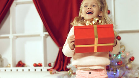 Cute little girl coming to the Christmas tree and looks at her New Year's giftの写真素材