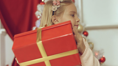 Blue-eyed little blonde girl is delighted from her New Year's gift wrapped in red paperの写真素材