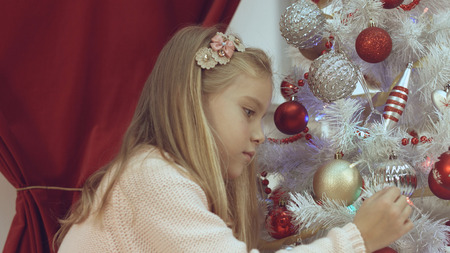 Little girl decorates the Christmas tree with bright toysの写真素材