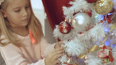 Adorable little blue-eyed girl decorates the Christmas tree with ballsの写真素材