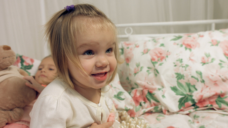 Adorable little girl sitting on a bed with her sisterの写真素材