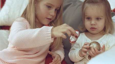 Two little sisters playing with Christmas balls while sitting on the couchの写真素材