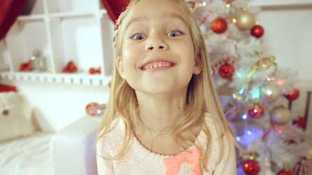 Happy little girl rejoices with a gift near the Christmas treeの写真素材