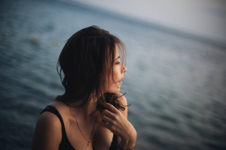 Sexy young woman in the black dress posing by the sea