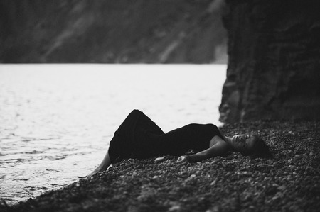 Sexy young woman in black skin-tight dress lying on the beach in waterの写真素材