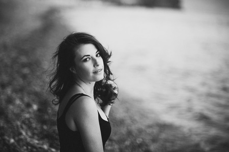 Amazing girl in the black dress sitting on the shore of the beachの写真素材