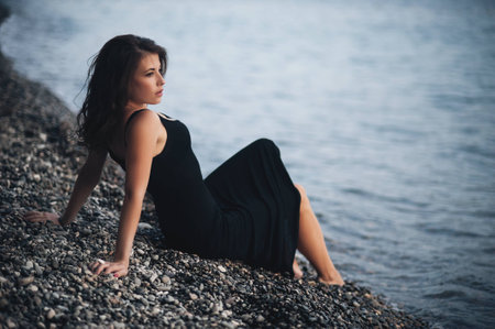 Sexy young woman in black skin-tight dress lying on the beach in waterの写真素材