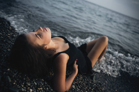 Attractive girl in the black wet dress lying on the shoreの写真素材