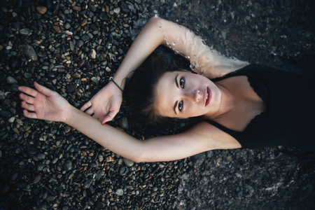 Attractive girl in the black wet dress lying on the shoreの写真素材