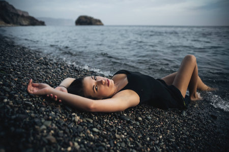 Attractive girl in the black wet dress lying on the shoreの写真素材