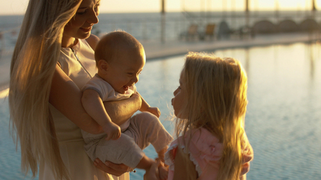 Mother with small children standing by the pool at sunsetの写真素材
