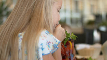 Little white-haired girl drinking berry lemonade with mint from the glassの写真素材
