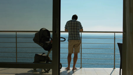 Family with baby carriage standing on the balcony and admiring the view of the seaの写真素材