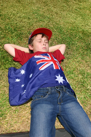 Patriotic Australian boy with Australian flag taking a short rest on grassy area.の写真素材