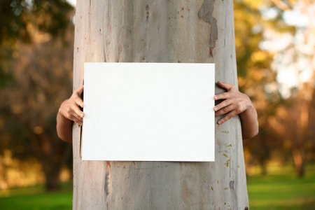 Environmentalist protester arms hugging large tree trunk and holding a blank sign ready for any message or statementの写真素材