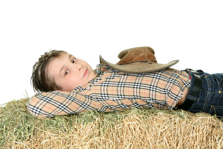 Country boy in checked shirt and jeans rests on a bale of lucern hay.の写真素材
