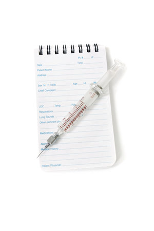 A medical notebook used my doctors and emergency services personnel and syringe needle on a white background.の写真素材