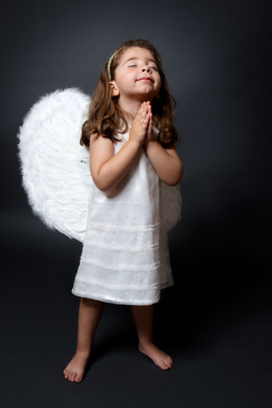 Little barefoot angel in white dress and feathered wings with hands together in quiet prayerの写真素材
