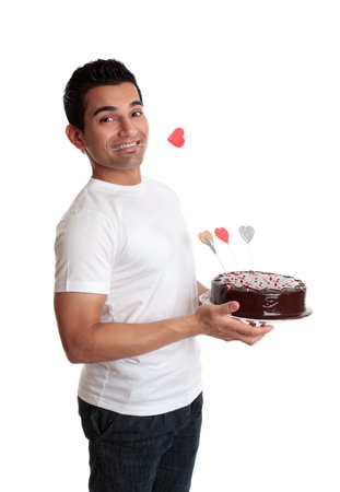 Cheeky flirtatious man carries a chocolate cake decorated with love hearts.    He has one heart clenched between his teeth.  Valentines, birthday or special occasion.  Side view against a white backdrop.の写真素材