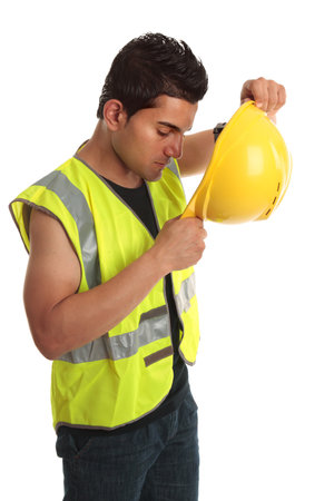 Builder construction worker putting on yellow protective hard hat.  He is also wearing a high...